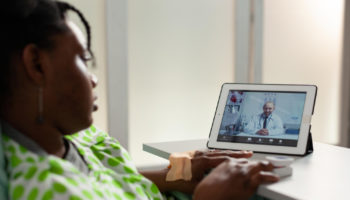 african-american-sick-woman-patient-lying-bed-discussing-medication-treatment-with-remote-physician-doctor-during-online-videocall-meeting-conference-telehealth-call-tablet-screen