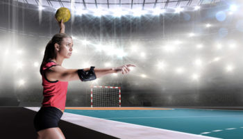 female-athlete-with-elbow-pad-throwing-handball-against-handball-field-indoor